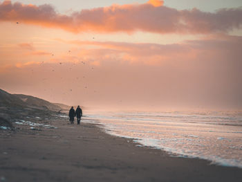 Silhouette couple walking at beach against sky during sunset