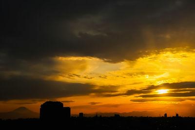 Silhouette buildings against dramatic sky during sunset