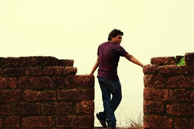 Young man standing against brick wall against clear sky