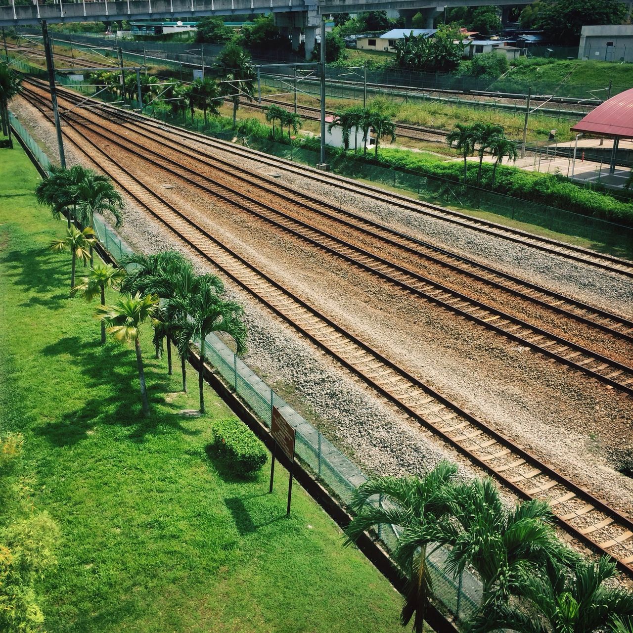 high angle view, green color, agriculture, grass, railroad track, field, rail transportation, landscape, growth, farm, rural scene, built structure, tree, transportation, building exterior, architecture, plant, nature, day, outdoors