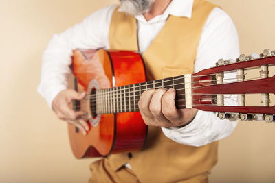 Close-up of a man playing acoustic guitar on a yellow wall.