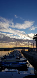 Boats moored in harbor at sunset