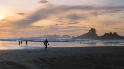 Silhouette people walking at beach against sky during sunset