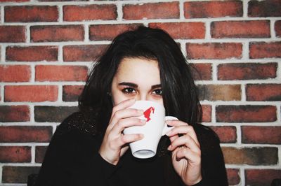 Portrait of young woman drinking coffee against brick wall