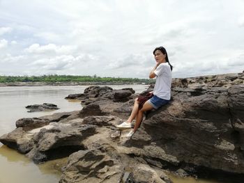 Full length of young woman on rock at beach against sky