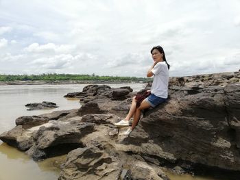 Woman sitting on rock at beach against sky