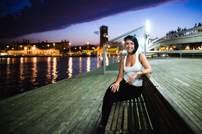 Portrait of woman sitting on bridge over city against sky