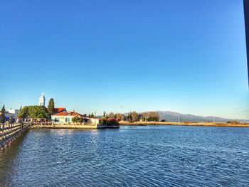 View of buildings by river against blue sky