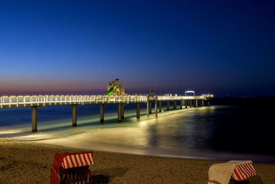 Illuminated pier over sea against blue sky
