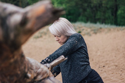 Side view of woman by fallen tree at forest