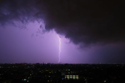 Lightning over illuminated cityscape against dramatic sky