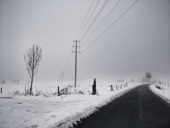 Empty road on snow covered landscape against sky