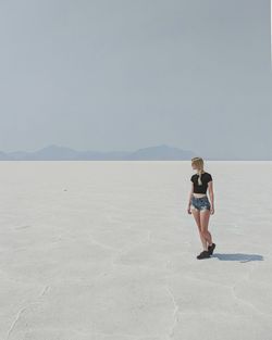 Woman walking on salt flat against clear sky