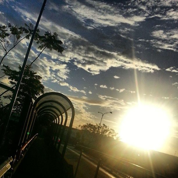 sky, sun, sunbeam, cloud - sky, sunlight, transportation, tree, lens flare, built structure, sunset, low angle view, the way forward, nature, cloud, architecture, cloudy, road, no people, silhouette, outdoors