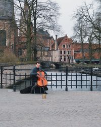 Portrait of young man playing cello on bridge in city