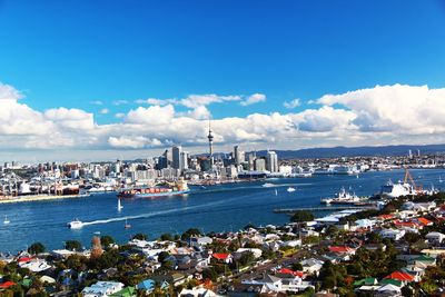 Aerial view of cityscape by sea against cloudy sky during sunny day