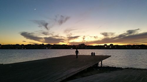 Silhouette people on calm lake in front of orange sky