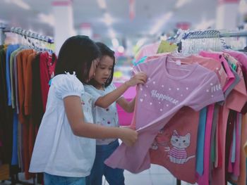 Little girls taking a look on beautiful children's clothes to choose at a supermarket.