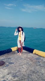 Full length of young woman standing at sea shore against sky