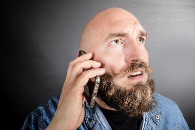 Thoughtful man talking on mobile phone against wall