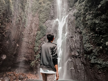 Rear view of man looking at waterfall in forest