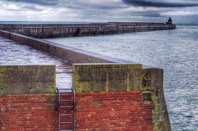 Pier on sea against cloudy sky