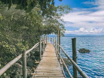 Wooden walkway by sea against sky