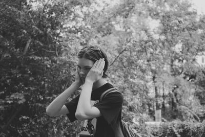 Teenage boy covering ears while standing against trees