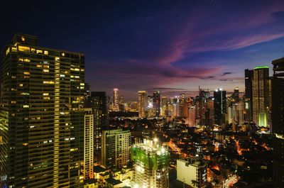 Illuminated modern buildings in city against sky at night