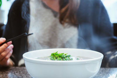 Midsection of woman having soup in bowl on table