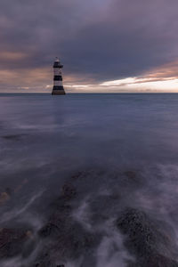 Lighthouse by sea against sky during sunset