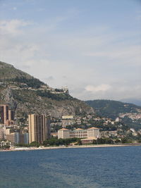 Buildings at sea shore by mountain against sky