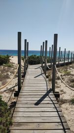 Wooden walkway leading towards sea against clear sky