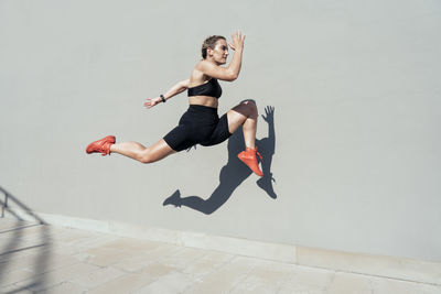 Young woman sprinting by wall on sunny day