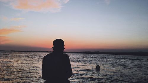 Rear view of silhouette man standing at beach during sunset