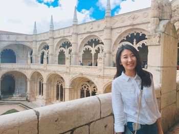 Portrait of smiling young woman standing against building and sky