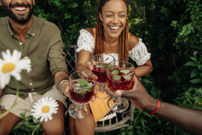 Cheerful male and female friends toasting drinks during garden party