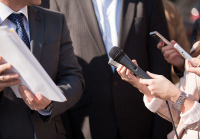 Midsection of journalist holding microphone in front of businessmen