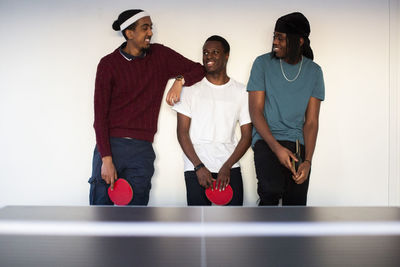 Smiling male friends standing against white wall in games room