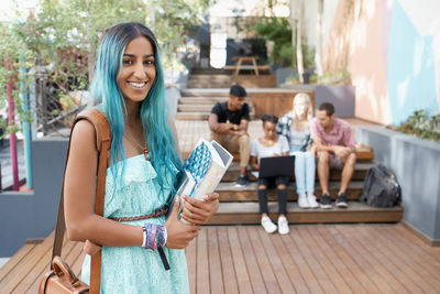 Portrait of young woman holding book with friends in background