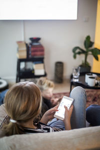 Rear view of girl using smart phone while sitting on sofa at home