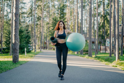 Woman with exercise mat and ball walking on road