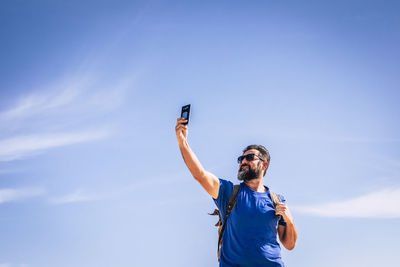 Low angle view of man taking selfie standing against blue sky