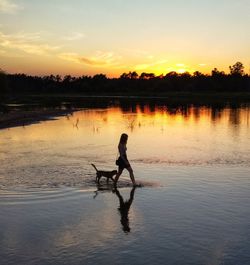 Silhouette man in lake against sky during sunset