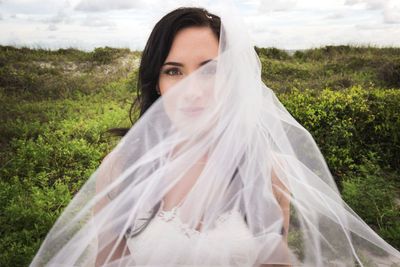 Portrait of bride standing on field against cloudy sky