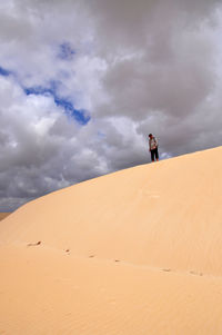 Low angle view of man standing at desert against cloudy sky