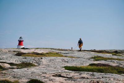 Rear view of man with dog walking towards lighthouse on mountain
