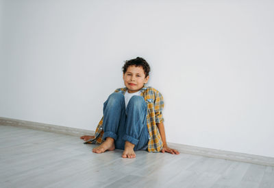 Portrait of crying boy sitting on floor against wall at home
