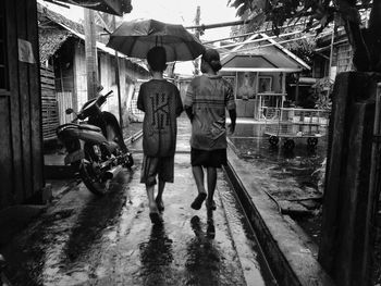 Rear view of people walking on wet road during rainy season