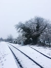 Snow covered railway tracks by bare trees against clear sky